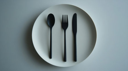 A minimalist table setup with sleek black spoon and fork on a matte white plate.の素材