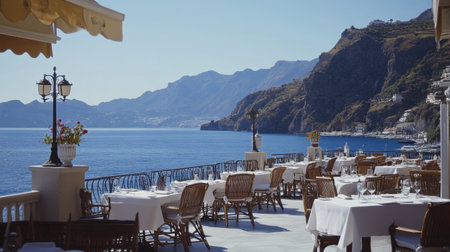 Enjoy a stunning coastal view from a terrace dining area featuring elegant tables overlooking the serene ocean and majestic mountains on a clear day.の素材