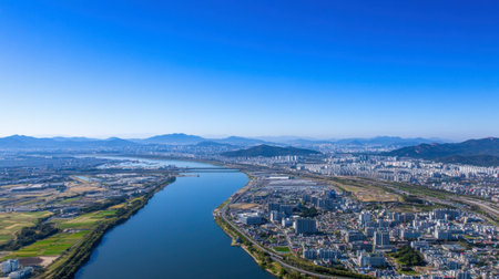 Experience a captivating aerial view showcasing a tranquil river, surrounded by vibrant greenery and urban landscapes, all under a brilliant blue sky for serene natural beauty.の素材