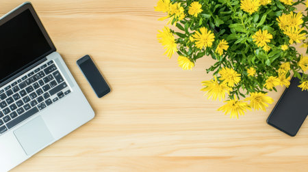 Bright and inviting workspace featuring a laptop, two smartphones, and vibrant yellow flowers set against a light wooden background, ideal for enhancing productivity and creativity.の素材