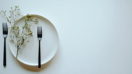A clean and minimalist dinner setting featuring a white plate with black forks and delicate green foliage, perfect for elegant dining experiences and culinary presentations.の素材