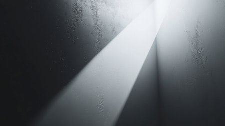 A dramatic light beam pierces through a dark corner, creating striking shadows and textures on a gray wall. Evokes feelings of serenity and mystery.の素材