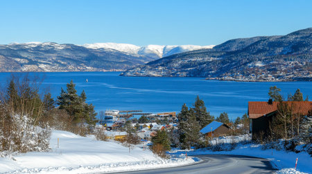 A breathtaking winter scene showcasing snow-covered mountains overlooking a tranquil lake. The clear blue sky enhances the serene atmosphere of this rural landscape.の素材