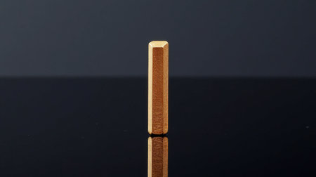 A golden hexagonal prism stands upright on a reflective black surface, showcasing its smooth texture and modern design against a minimalistic background.の素材