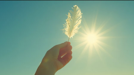 A serene image of a hand holding a delicate feather against a bright sunlight backdrop. This visual captures themes of peace, freedom, and nature, evoking feelings of tranquility and hope. Perfect for wellness and inspirational content.の素材