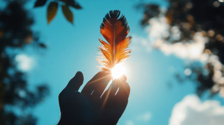 A hand holding a glowing feather against a vibrant blue sky. This image captures the essence of nature's beauty and serenity, evoking feelings of freedom and inspiration.の素材