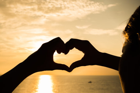 Silhouette hand woman heart on sunset the sea
