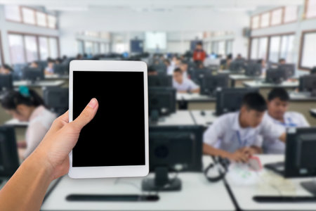 Hands are holding touch screen White Tablet Computer on student study computer classroom for...
