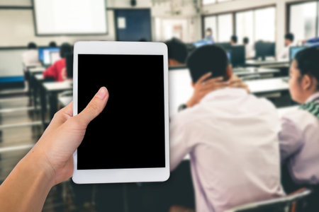 Hands are holding touch screen White Tablet Computer on student study computer classroom for background.の写真素材