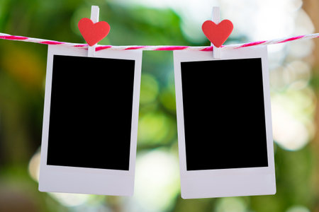 2 Blank instant photo and red clip paper heart hanging on the clothesline with nature bokeh background..Designer concept.の写真素材