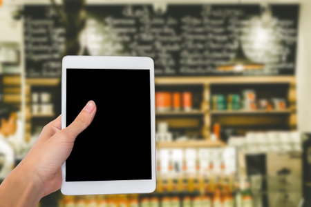 Hands are holding touch screen White Tablet Computer on blurred shopping super market background.の写真素材