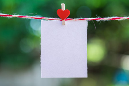 Blank white paper and red clip paper heart hanging on the clothesline with bokeh nature...