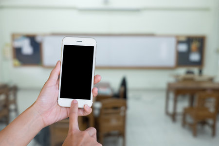 Hands woman are holding touch screen smart phone,tablet on blurred classroom nobody student and teacher  background.の写真素材
