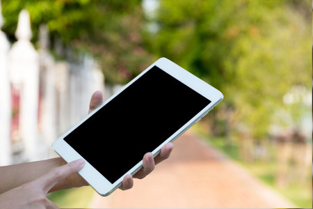 Hands woman are holding touch screen smart phone,tablet on blurred walkway garden nature background.