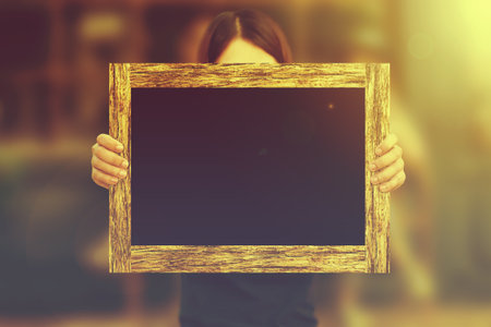 Woman holding blackboard wooden frame with nature background.Vintage or retro tone.Business conceptの写真素材