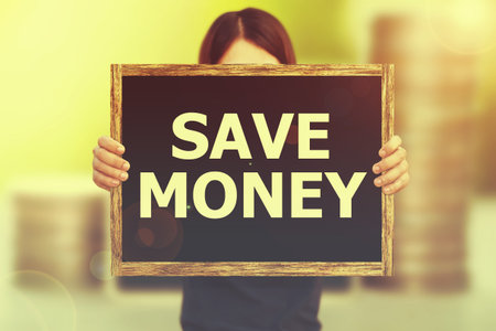 SAVE MONEY message on the blackboard wooden frame on hand woman with blurred coins tower with nature background. business and saving money concept. Vintage or retro tone.の写真素材