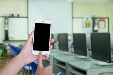 Hands woman are holding touch screen smart phone,tablet on blurred Defocused computer classroom  background.の写真素材