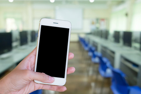 Hands woman are holding touch screen smart phone,tablet on blurred Defocused computer classroom  background.の写真素材