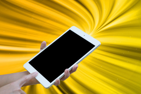 Hands woman are holding touch screen White Tablet on blurred Gold glitter sparkle defocused radial rays twinkled lights bokeh beautiful abstract background.の写真素材