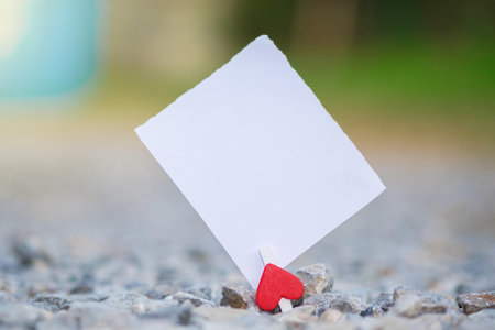 Blank white paper and red clip paper heart hanging on the many stone with bokeh nature background.Designer concept.の写真素材