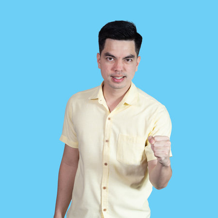 Portrait handsome young asian man wearing a yellow shirt showing excitement or celebrating  sign isolated on blue background. Asian man people. business success concept.の写真素材