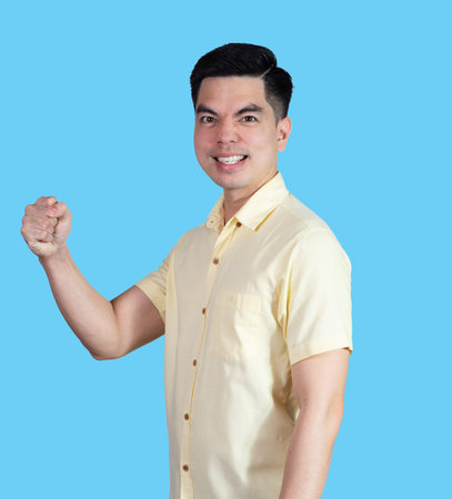 Portrait handsome young asian man wearing a yellow shirt showing excitement or celebrating  sign isolated on blue background. Asian man people. business success concept.の写真素材