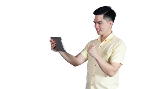 Portrait handsome young asian man wearing a yellow shirt holding smart phone or tablet feeling celebrating or successful isolated on blue background. Businessman concept. Asia people.の写真素材