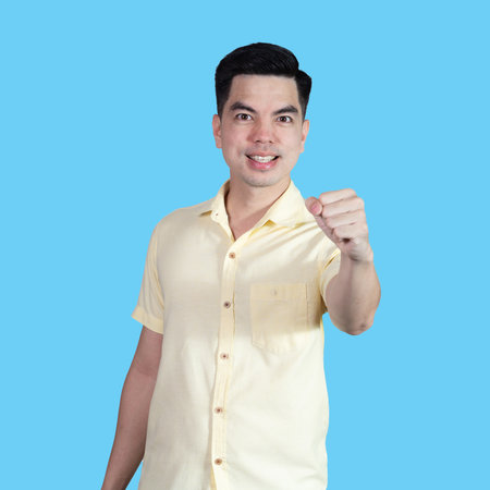 Portrait handsome young asian man wearing a yellow shirt showing excitement or celebrating  sign isolated on blue background. Asian man people. business success concept.の写真素材