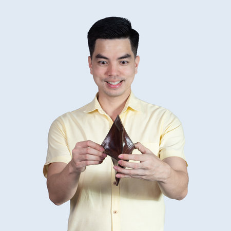 Portrait Handsome young asian man wearing a yellow shirt surpise money in the wallet isolated on blue background. Asia people.の写真素材