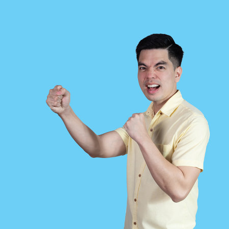 Portrait handsome young asian man wearing a yellow shirt showing excitement or celebrating  sign isolated on blue background. Asian man people. business success concept.の写真素材