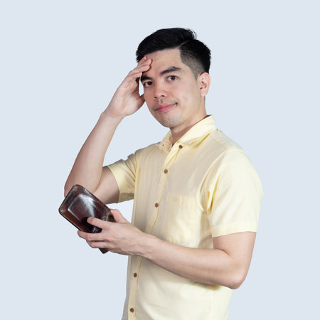 Portrait Handsome young asian man wearing a yellow shirt stressed because empty wallet no money isolated on white background. Asia people.の写真素材