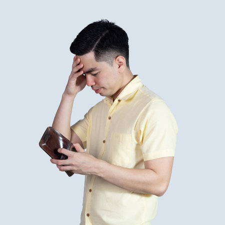Portrait of a handsome young Asian man wearing a yellow shirt, looking stressed due to an empty wallet, isolated on a white background.の写真素材