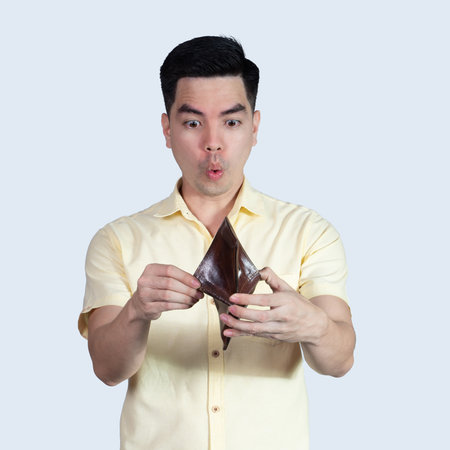Portrait Handsome young asian man wearing a yellow shirt surprise money in the wallet isolated on blue background.の写真素材