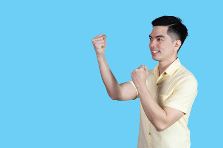 Portrait handsome young asian man wearing a yellow shirt showing excitement or celebrating  sign isolated on blue background. Asian man people. business success concept.の写真素材