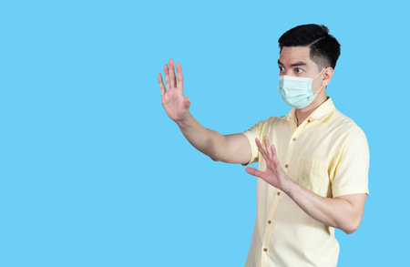 Portrait handsome young asian man wearing yellow shirt and mask protection isolated on blue background in studio. Asian man people.の写真素材