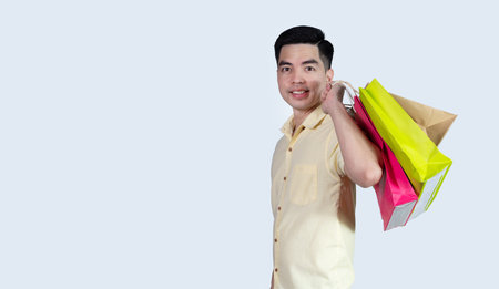 Portrait handsome young asian man wearing yellow cheerful glad content guy carrying new things colorful packages on gray background in studio. Asian man people.の写真素材