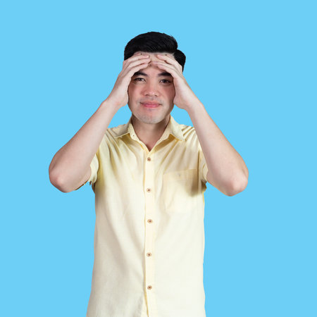 Portrait handsome young asian man wearing a yellow shirt stressed and anxiety sign isolated on blue background in studio.Asian man people.business concept.の写真素材