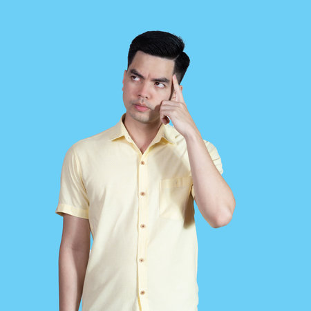 Portrait handsome young asian man wearing a yellow shirt thinking isolated on blue background in studio.Asian man people.business concept.の写真素材