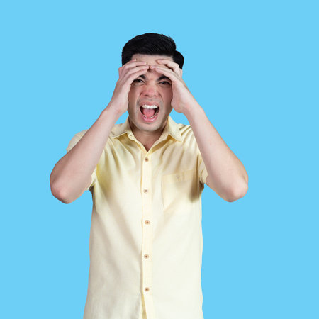 Portrait handsome young asian man wearing a yellow shirt stressed and anxiety sign isolated on blue background in studio.Asian man people.business concept.の写真素材