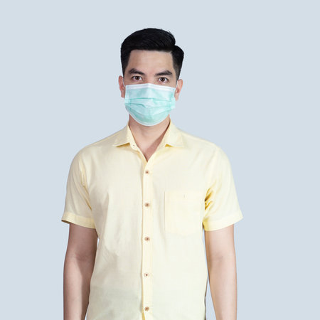 COVID-19 Coronavirus portrait handsome young asian man wearing yellow shirt and mask protection from covid 19 isolated on grey background in studio. Asian man people. COVID-19 concept.の写真素材