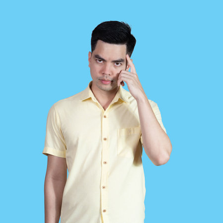 Portrait handsome young asian man wearing a yellow shirt thinking isolated on blue background in studio.Asian man people.business concept.の写真素材