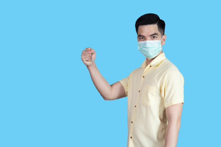FIGHT! virus portrait handsome young asian 
man wearing yellow shirt and mask protectionの写真素材