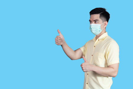 portrait handsome young asian man wearing yellow shirt and maskの写真素材