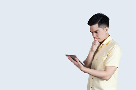 Terrible headache. portrait handsome young asian man wearing a yellow shirt holding smart phone or tablet feeling stressful isolated on white background. Businessman concept. Asia people.の写真素材