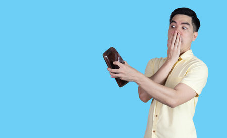 Portrait Handsome young asian man wearing a yellow shirt stressed because empty wallet no money isolated on blue background. Businessman concept. Asia people.の写真素材