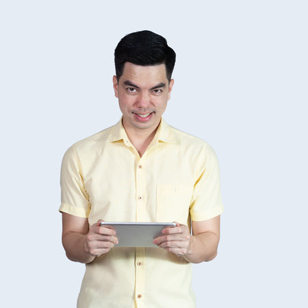 Terrible headache. portrait handsome young asian man wearing a yellow shirt holding smart phone or tablet feeling stressful isolated on blue background. Businessman concept. Asia people.の写真素材