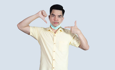COVID-19 Coronavirus close up handsome young asian man wearing yellow shirt holding tablet and mask protection from covid 19 isolated on white background in studio. Asian man people.の写真素材