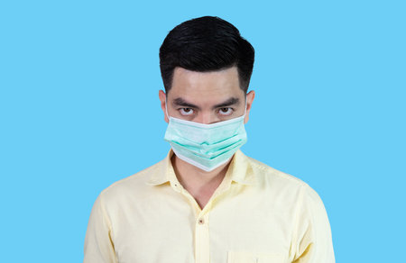 COVID-19 Coronavirus close up handsome young asian man wearing yellow shirt holding tablet and mask protection from covid 19 isolated on white background in studio. Asian man people.の写真素材