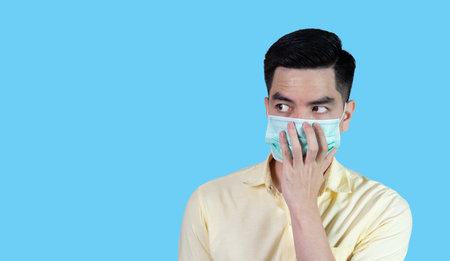 COVID-19 Coronavirus close up handsome young asian man wearing yellow shirt holding tablet and mask protection from covid 19 isolated on white background in studio. Asian man people.の写真素材