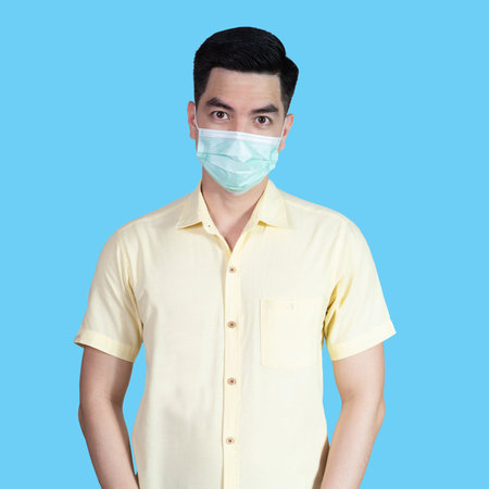 COVID-19 Coronavirus close up handsome young asian man wearing yellow shirt holding tablet and mask protection from covid 19 isolated on white background in studio. Asian man people.の写真素材
